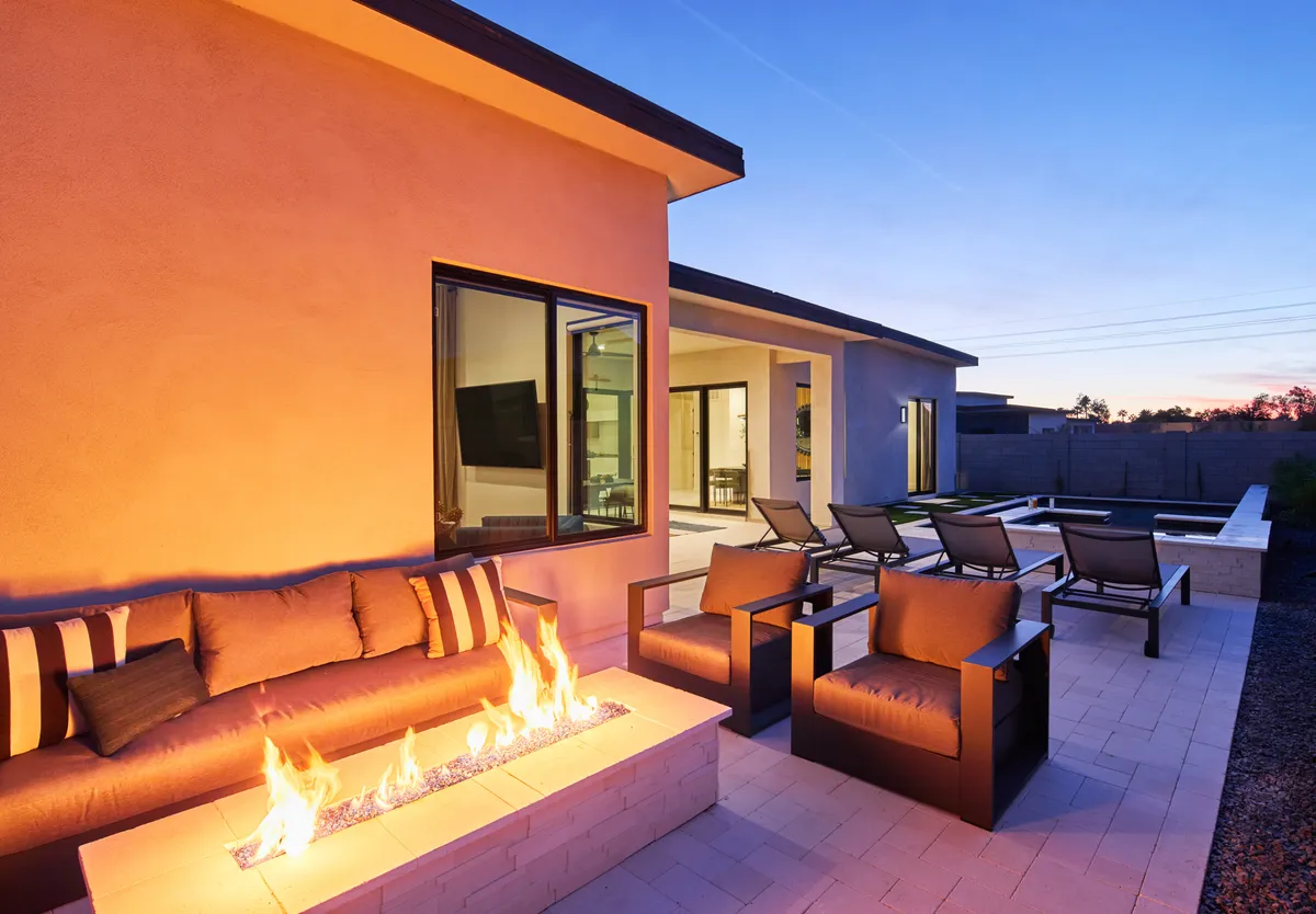 An intimate evening scene with a glowing fire pit surrounded by a cozy seating area, all set beside the illuminated pool. The background reveals the serene pool area, perfect for gatherings under the stars.
