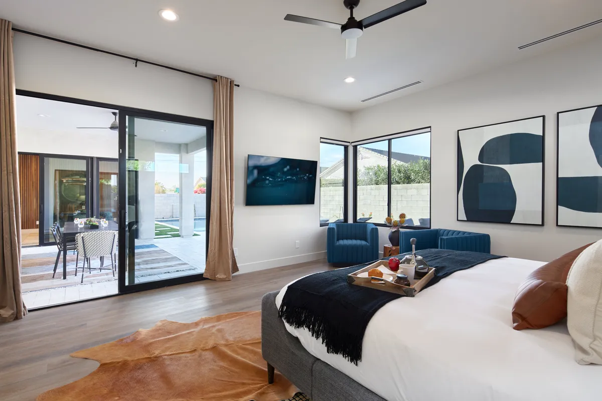 A cozy, modern bedroom with a bed featuring an accent pillow, a coffee tray with snacks, artwork on the wall, and large glass doors that open directly to the outdoors. Natural light floods the space, and the room feels welcoming and serene.