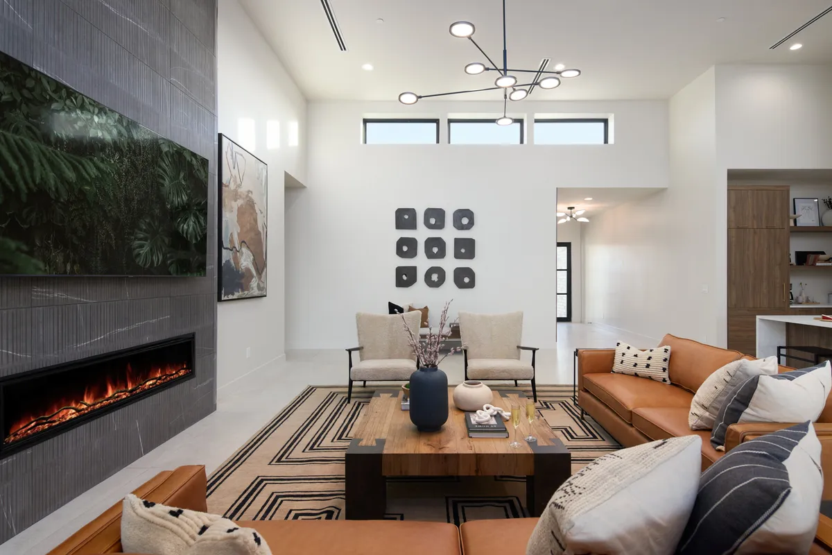 A sophisticated living space with a large piece of modern wall-mounted artwork, a striking chandelier, a cozy coffee table adorned with decor, and a fireplace that adds warmth to the room. The room radiates comfort and security, perfect for both gatherings and quiet relaxation.