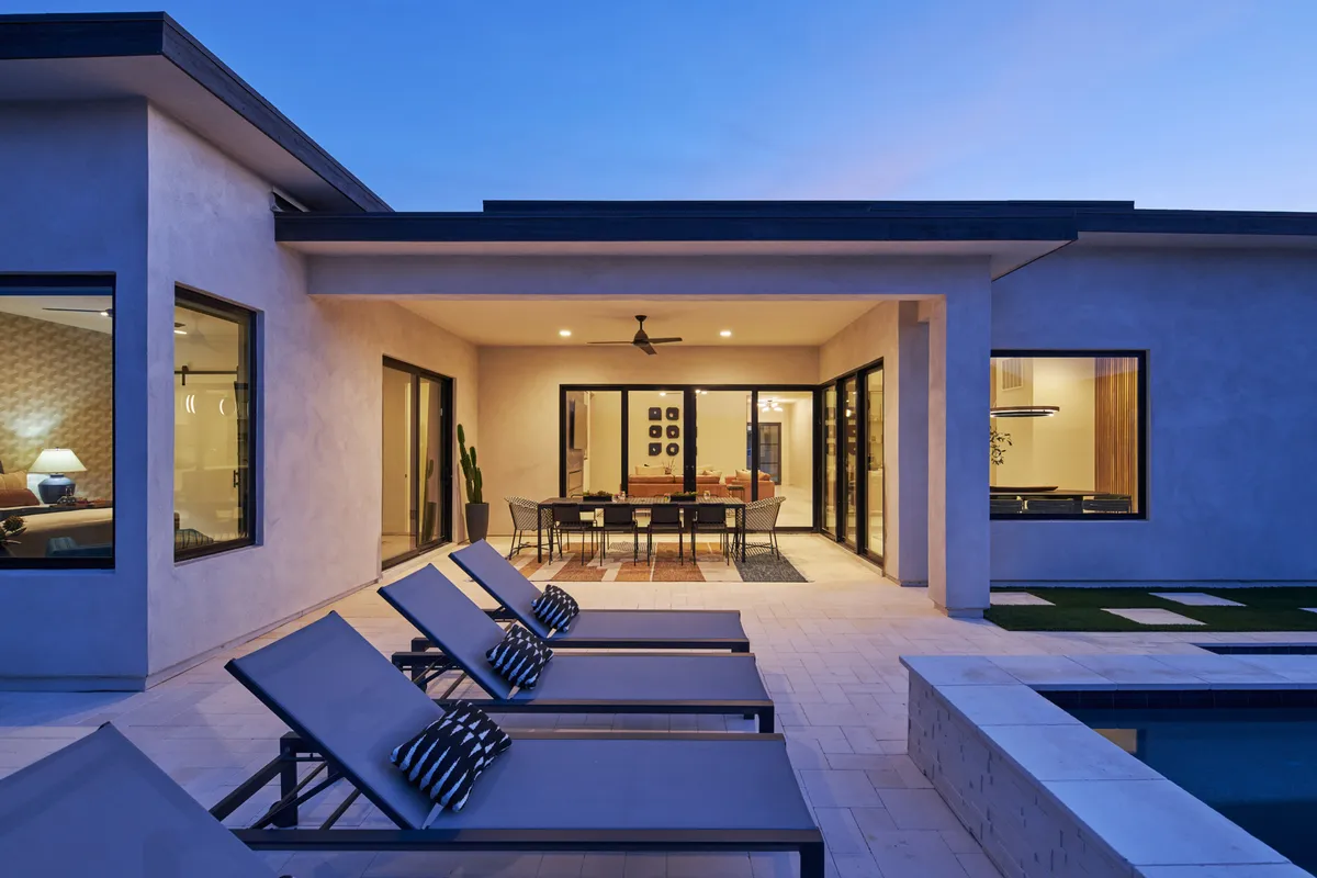 A stylish backyard featuring a sparkling swimming pool, modern lounge chairs, an outdoor dining table, and seamless sliding glass doors that connect the interior with the patio. The setting exudes tranquility and sophistication, ideal for both relaxation and team gatherings.