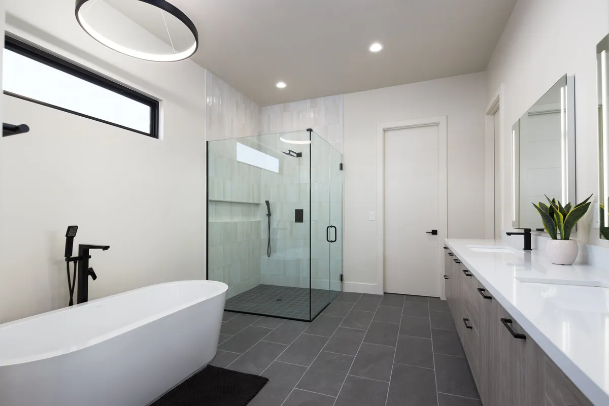 A luxurious bathroom with a freestanding soaking tub, glass shower enclosure, and dual sinks with elegant mirrors. The design is serene and spa-inspired, with a sense of openness and relaxation.