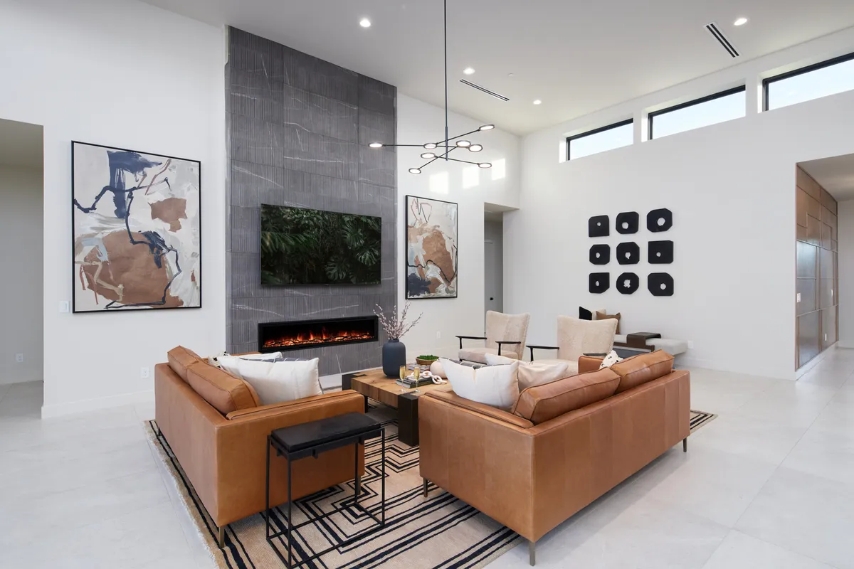 A contemporary living room featuring plush leather sofas arranged for conversation, a modern fireplace, and large wall art. The space is filled with natural light and greenery, creating a welcoming setting for relaxation or social gatherings.