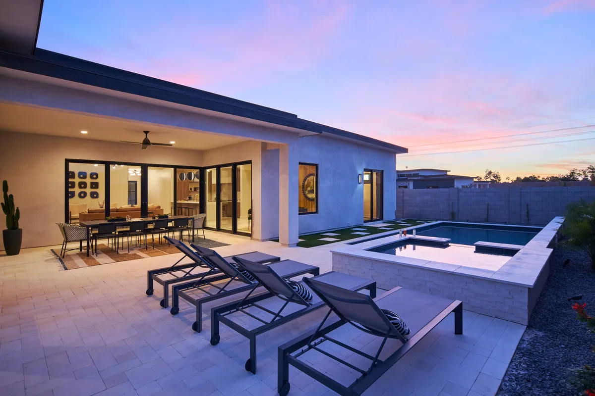 A tranquil backyard oasis featuring a sparkling swimming pool, lounge chairs, a shaded patio dining area, and lush landscaping. The setting is ideal for unwinding after a busy day of event attendance, evoking the promise of relaxation and luxury at Luna Luxe.