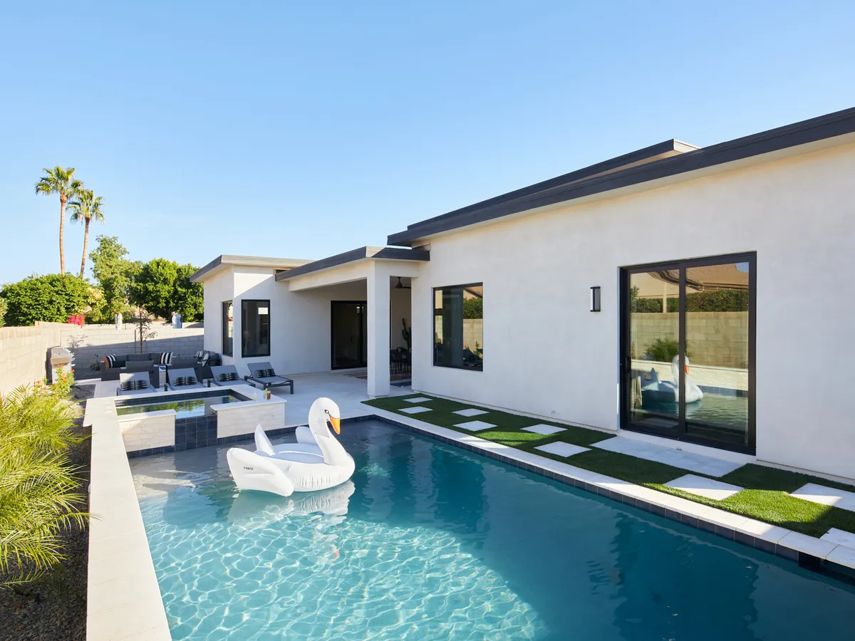 A lively outdoor scene showcasing a private swimming pool with a playful swan float, a comfortable outdoor seating area, and lush landscaped gardens. The mood is both tranquil and playful, emphasizing relaxation and social activities in a backyard setting.